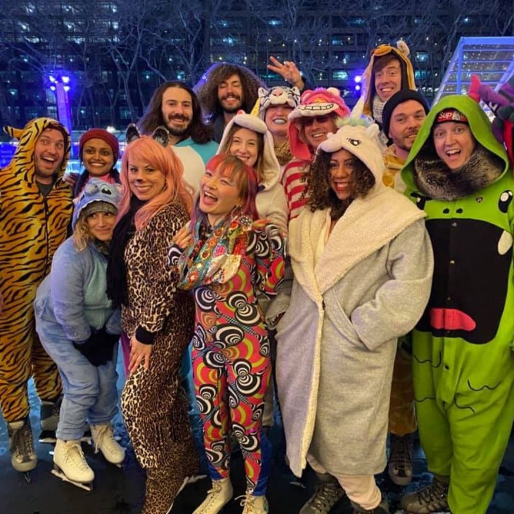 group of adults wearing onsies posing with ice skates