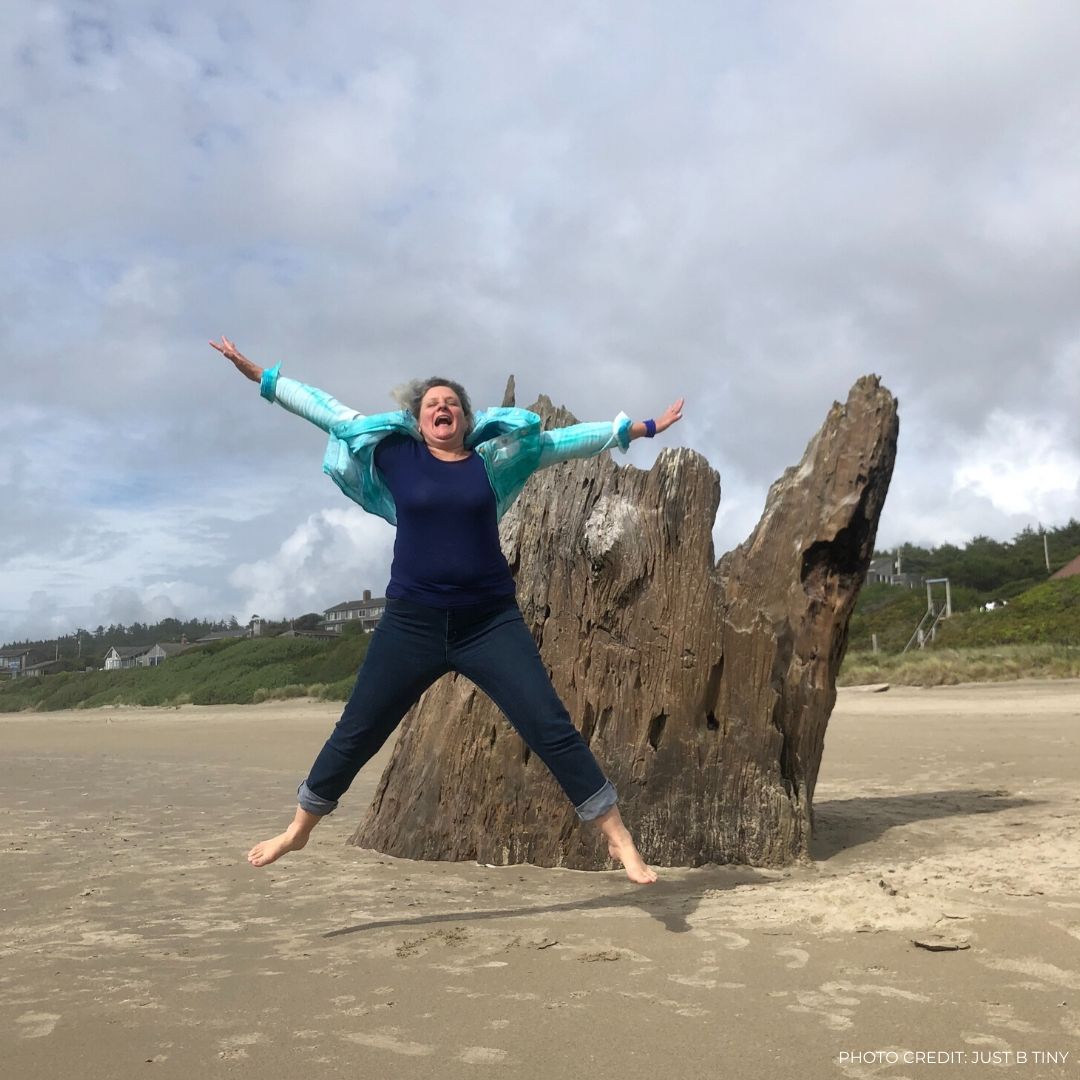 Me jumping in front of stump on beach across from tiny house park