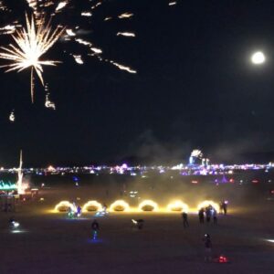 nighttime view of adventure mobiles lit up with fireworks and full moon in sky