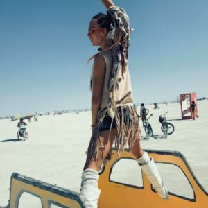Young woman with long hair standing on windows of taxi cab art at Burning Man